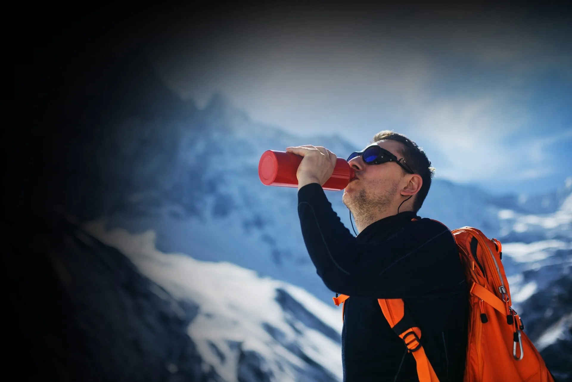 mand drinking from bottle with snow covered mountains in the background