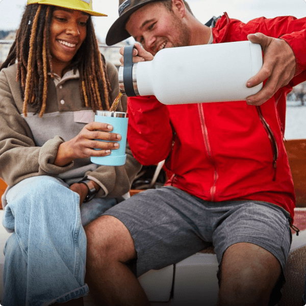 man pouring tea from flask into cup held by woman